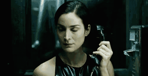 a woman is talking on a pay phone in a dark room and making a stop sign with her hand .