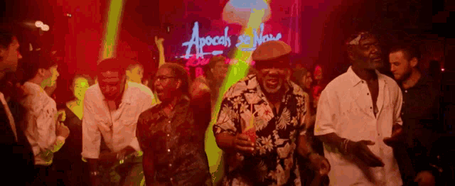 a group of people dancing in front of a sign that says apocalyptic now