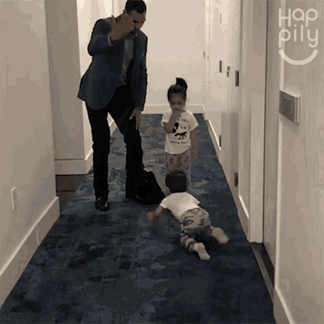a man in a suit is talking on a cell phone while two children play in a hallway .