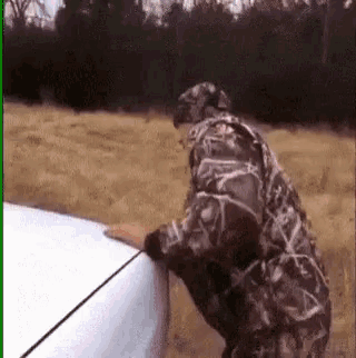 a man in a camo jacket is standing next to a white car .