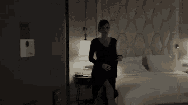 a woman in a black dress is standing in a hotel room next to a bed