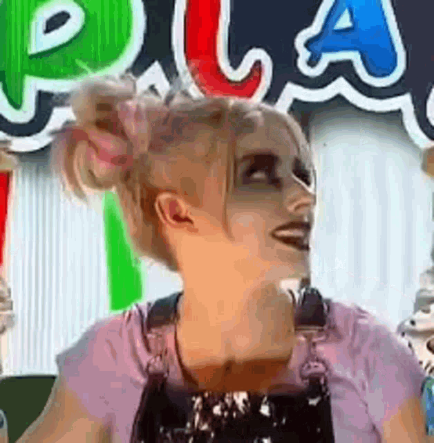 a woman wearing overalls and a pink shirt is smiling in front of a sign that says play