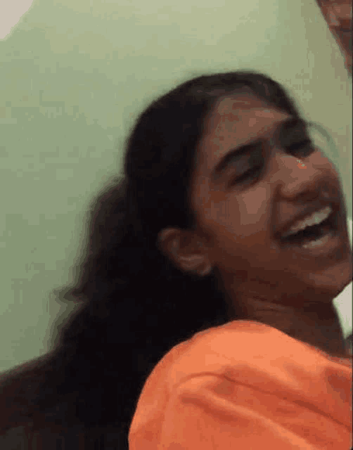 a young girl is laughing and making a funny face while wearing an orange shirt .