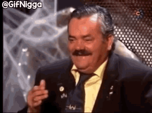 a man with a mustache is wearing a suit and tie and is laughing .