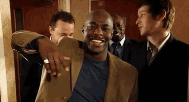 a group of men are standing around a man in a blue shirt