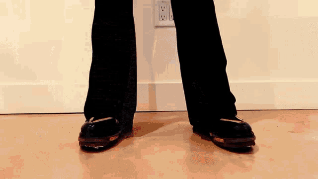 a person wearing black pants and black shoes standing on a wood floor