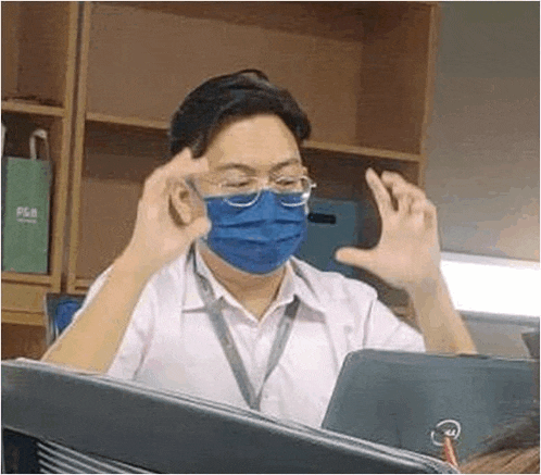 a man wearing a blue face mask and glasses is sitting in front of a laptop computer .