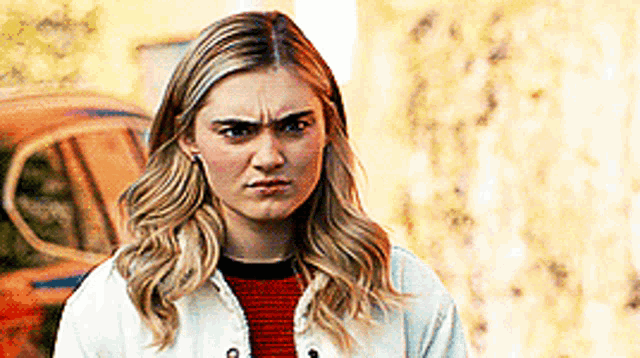 a woman in a white jacket and red sweater is making a funny face .