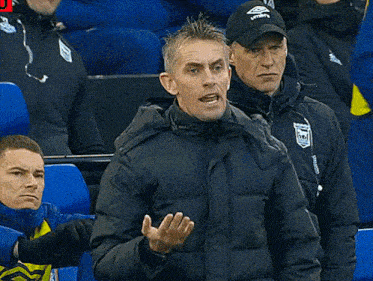 a man wearing a umbro hat stands in the stands