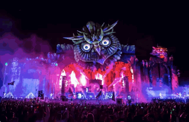 a crowd at a music festival with a giant owl on stage