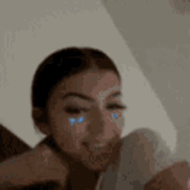 a woman with blue tears on her face is smiling while looking at a cell phone .