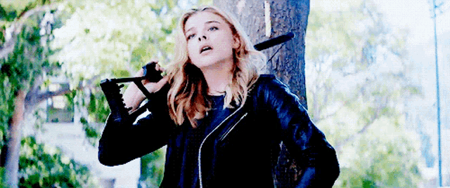 a woman in a leather jacket is holding a saw in her hand .