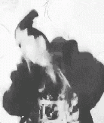 a black and white photo of a person smoking a cigarette with smoke coming out of their mouth .