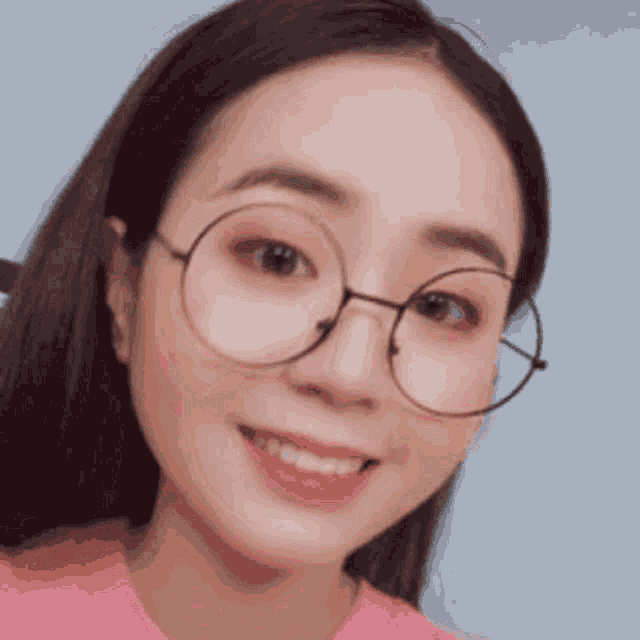 a woman wearing round glasses and a pink shirt smiles