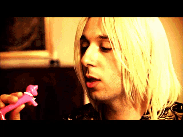 a man with long blonde hair is holding a pink toy in his hand
