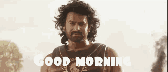 a man with a beard is standing in front of a sign that says " good morning "