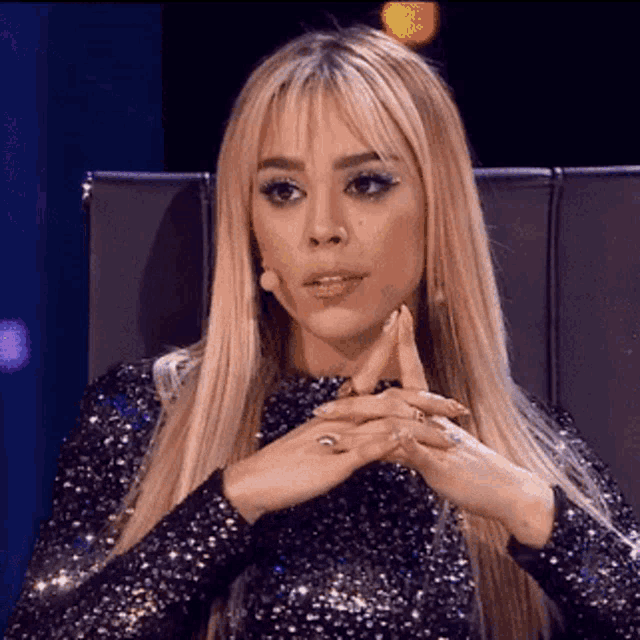 a woman with blonde hair is sitting in a chair with her hands folded and a microphone in her hand .