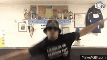 a man wearing a hat and sunglasses is dancing in front of a wall with trophies hanging on it .