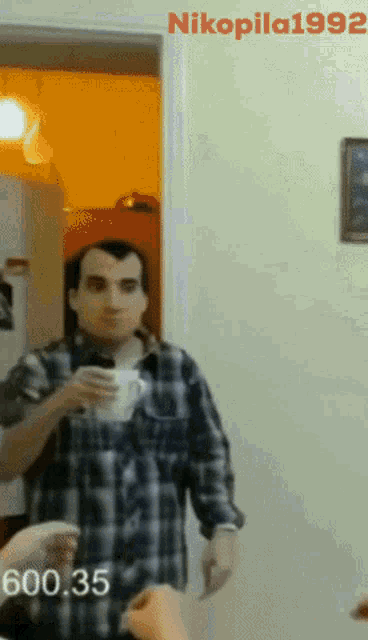 a man in a plaid shirt holds a cup of coffee in front of a door with nikopila1992 written on the bottom
