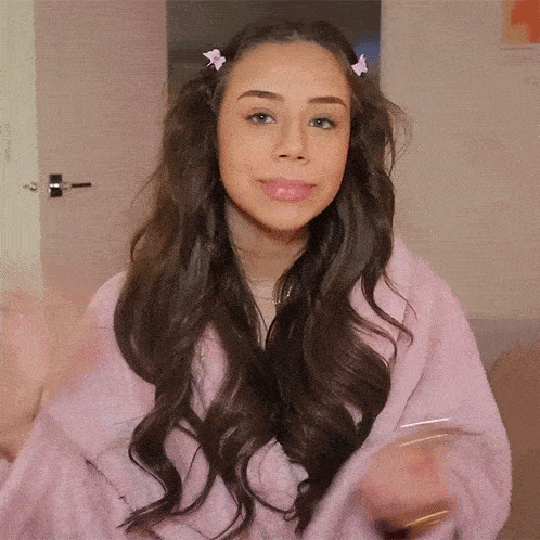 a woman with long brown hair is wearing a pink robe and a pink hair clip .