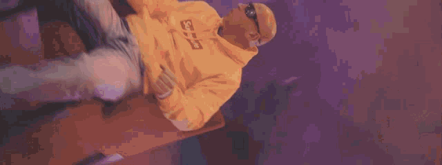a bald man wearing a yellow supreme hoodie