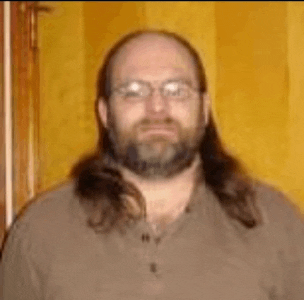 a man with long hair and a beard is wearing glasses and a brown shirt .