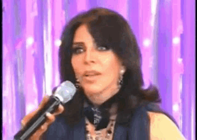 a woman is singing into a microphone in front of a purple curtain