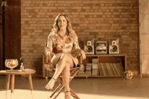 a woman is sitting in a chair with her legs crossed in front of a brick wall