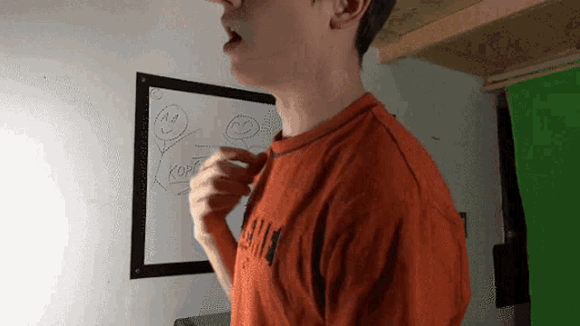 a man in an orange shirt is standing in front of a white board with a drawing of a face on it