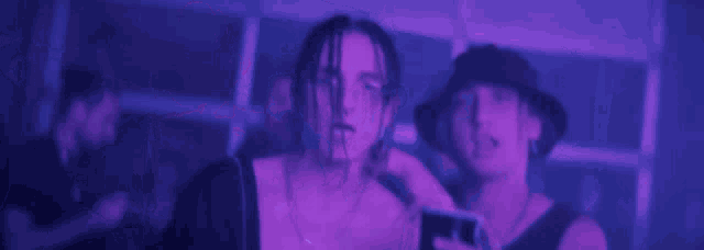 two men are standing next to each other in a dark room with purple lights