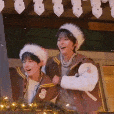 two young men wearing santa hats are standing next to each other and laughing .