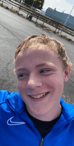 a young man wearing a blue nike jacket is smiling