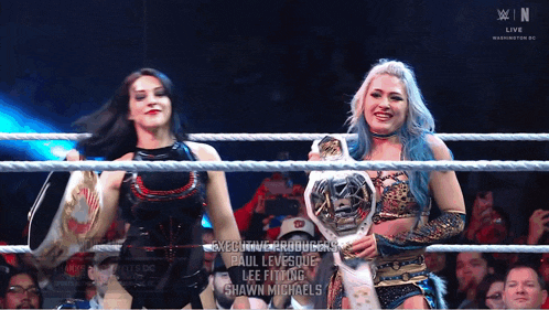 two women in a wrestling ring with executive producers paul levesque and lee fitling