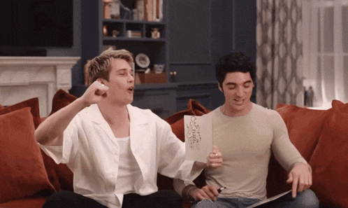 two men are sitting on a couch and one is holding a piece of paper that says " i love you "