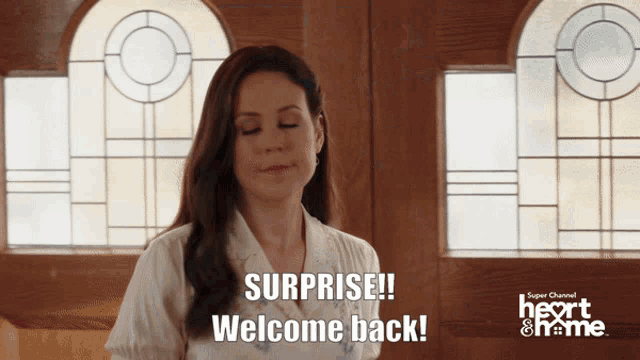 a woman is standing in front of a window and says surprise welcome back