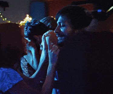 a man and a woman are kissing in front of a string of lights