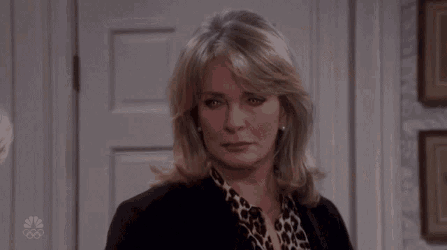 a woman wearing a leopard print shirt and a black jacket stands in front of a door that says nbc on it