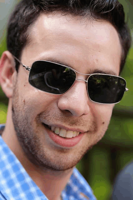 a man wearing sunglasses and a blue shirt smiles