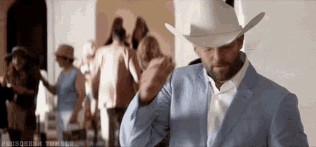 a man in a suit and cowboy hat is standing in front of a crowd