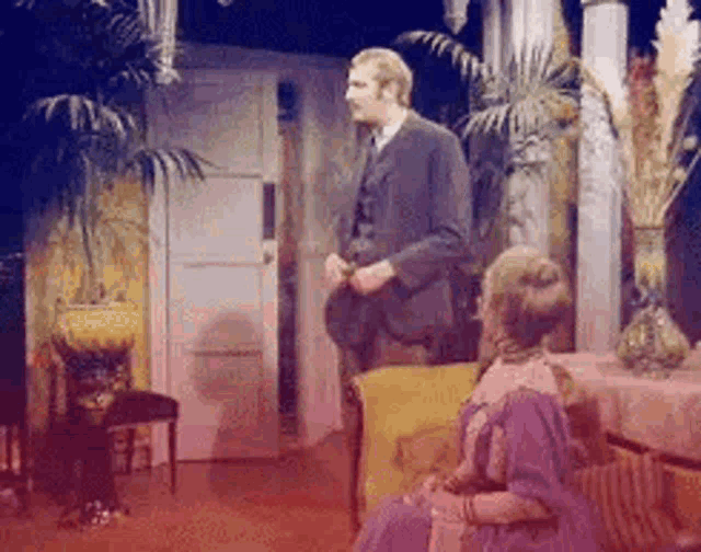 a man is standing next to a woman sitting on a couch in a living room .
