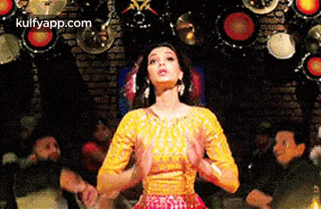a woman in a yellow top is dancing in front of a drum set in a room .