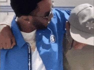 a man wearing a blue jacket is hugging another man wearing a hat