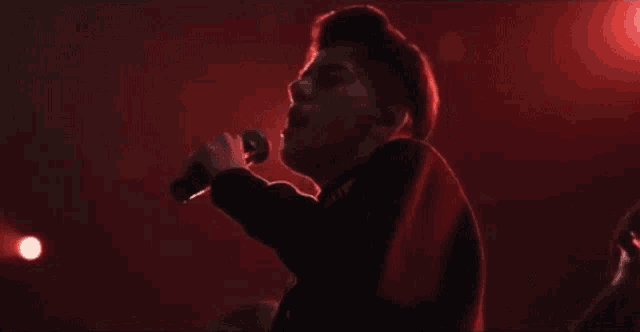 a man is singing into a microphone in front of a red light .