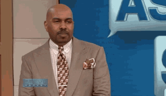 a man in a suit and tie is standing in front of a sign that says " steve harvey "