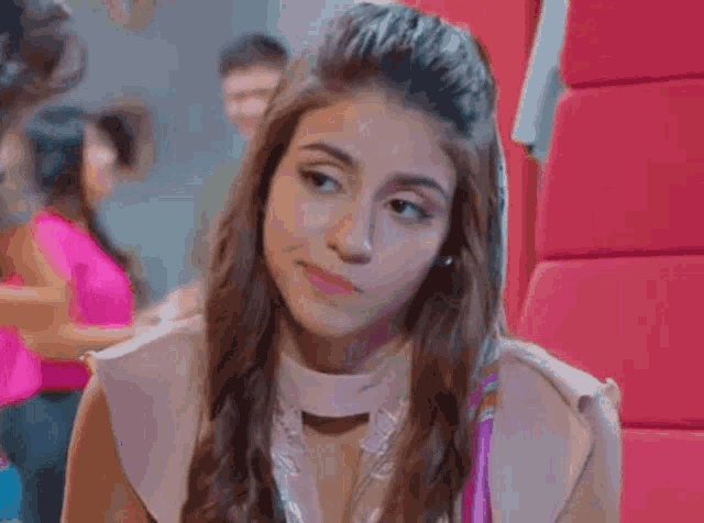 a young woman is sitting in front of a red wall and looking at the camera with a serious look on her face .