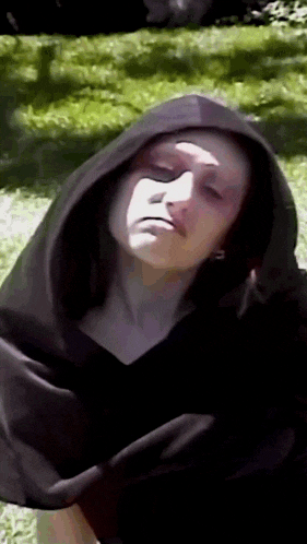 a woman wearing a black cape with a hood looks at the camera