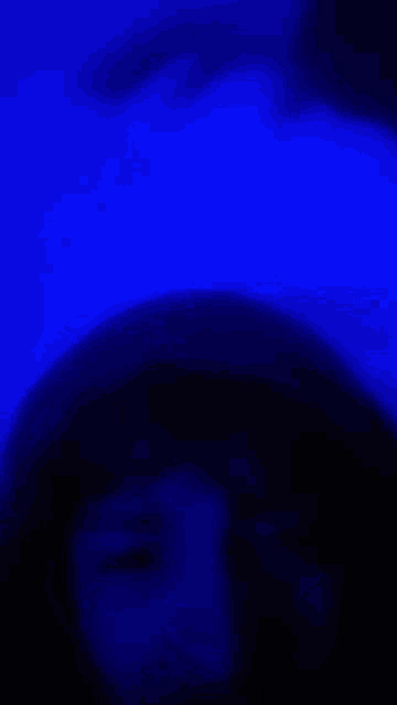 a blurry picture of a person 's face in a dark room with a blue light behind them .