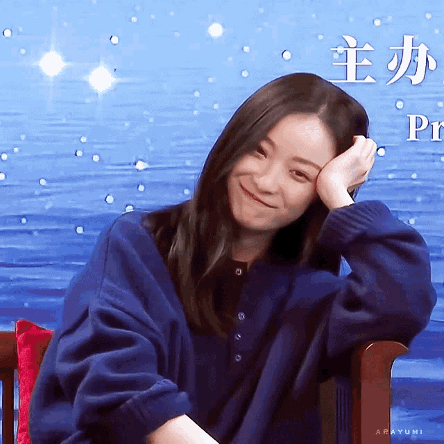 a woman in a blue sweater is smiling in front of a blue background with chinese writing