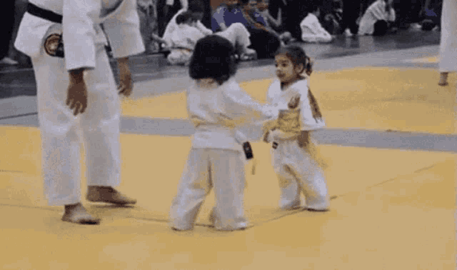 a person in a white kimono is standing next to a child in a white kimono on a wrestling mat .
