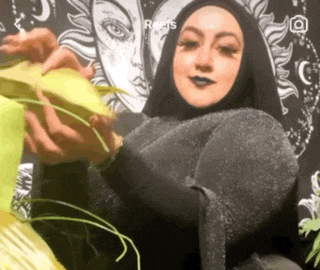a woman in a hijab is holding a piece of paper in front of a wall .